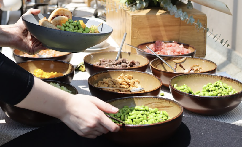 Estación de comida para banquete, con ingredientes frescos como edamames, proteínas y toppings, servidos al gusto.
