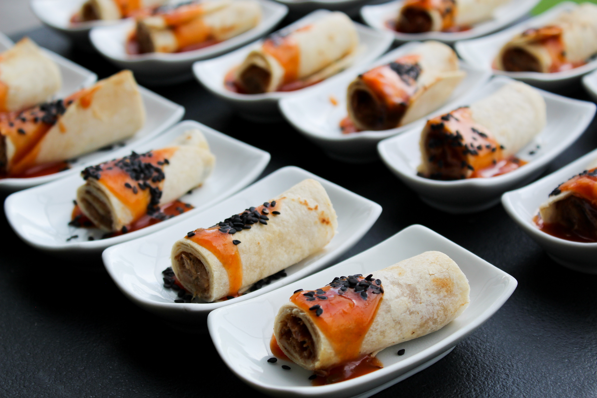 Canapés servidos en platos individuales, taquitos de pato con salsa agridulce y ajonjolí negro, ideales para banquete tipo cóctel.