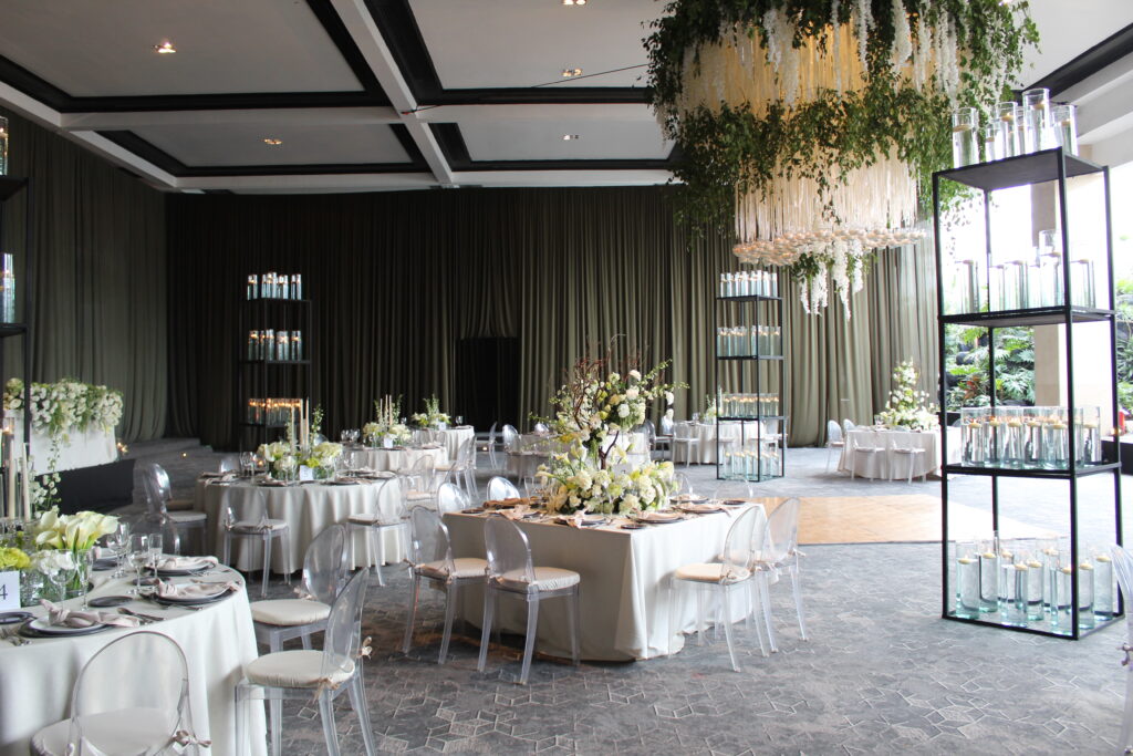 Montaje elegante de salón para banquete social con mesas redondas, flores blancas y sillas transparentes, ideal para bodas o eventos formales.