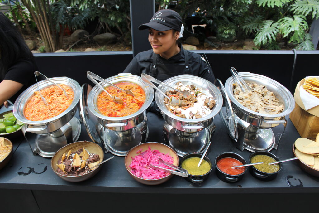 Buffet de banquete con platillos mexicanos, incluyendo guisos, salsas, frijoles y tortillas, atendido por chef de Ambrosía.