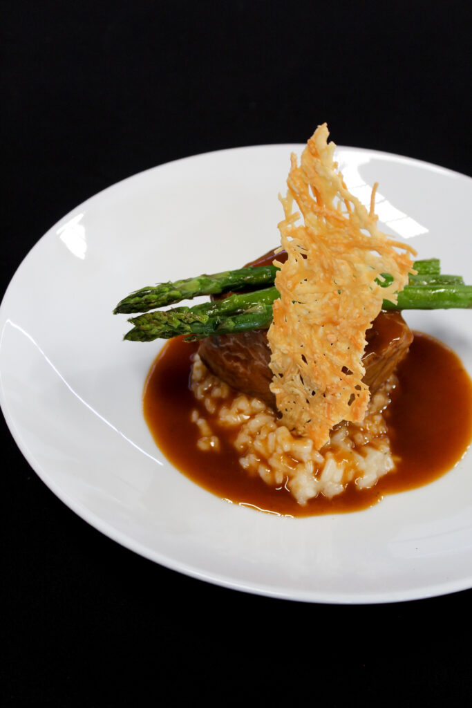 Platillo gourmet servido por Ambrosía con risotto, espárragos y crujiente de quesoFotografía de un platillo de alta cocina incluido en el servicio de catering para bodas de Ambrosía. Ideal para mostrar la calidad y presentación de los menús personalizados.